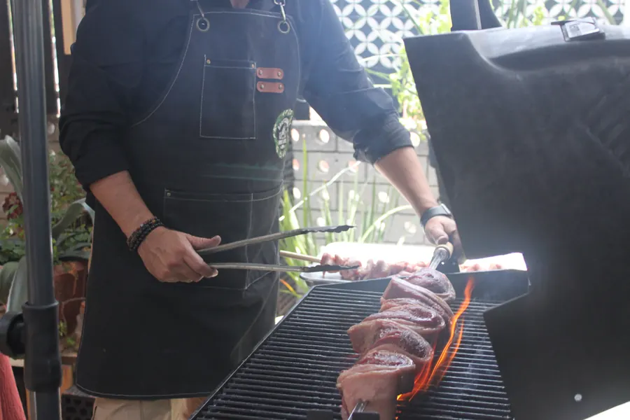 Chef girando un corte de carne sobre brasa viva con pinzas de hierro