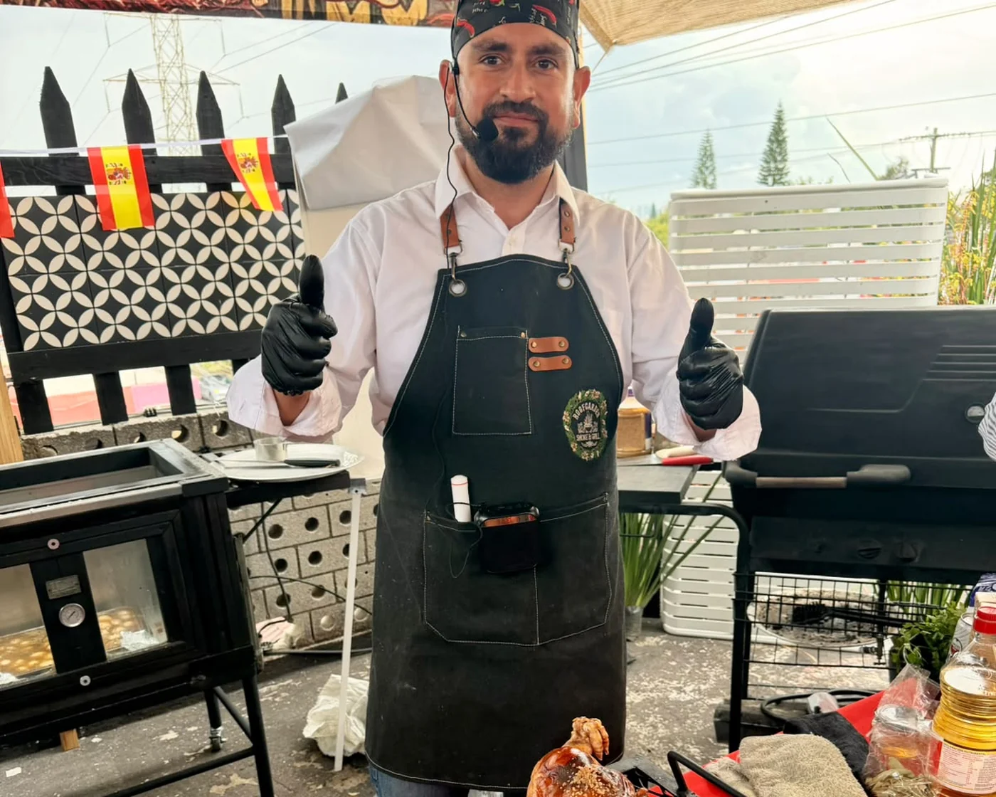 Chef de RoofGarden sonriendo con pulgares arriba junto a un lechón entero recién salido del fuego